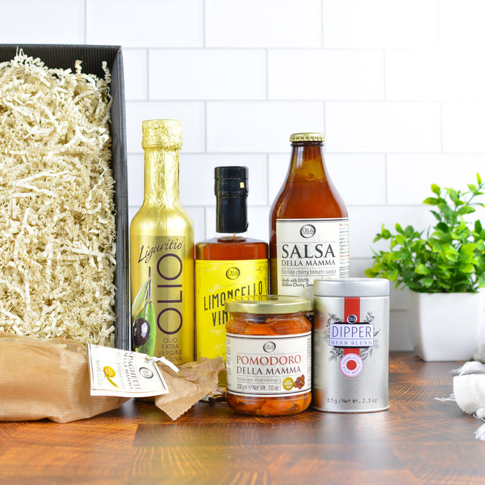 Assorted food products including pasta, oils, and other pantry items on a wooden surface with a white tiled wall background.