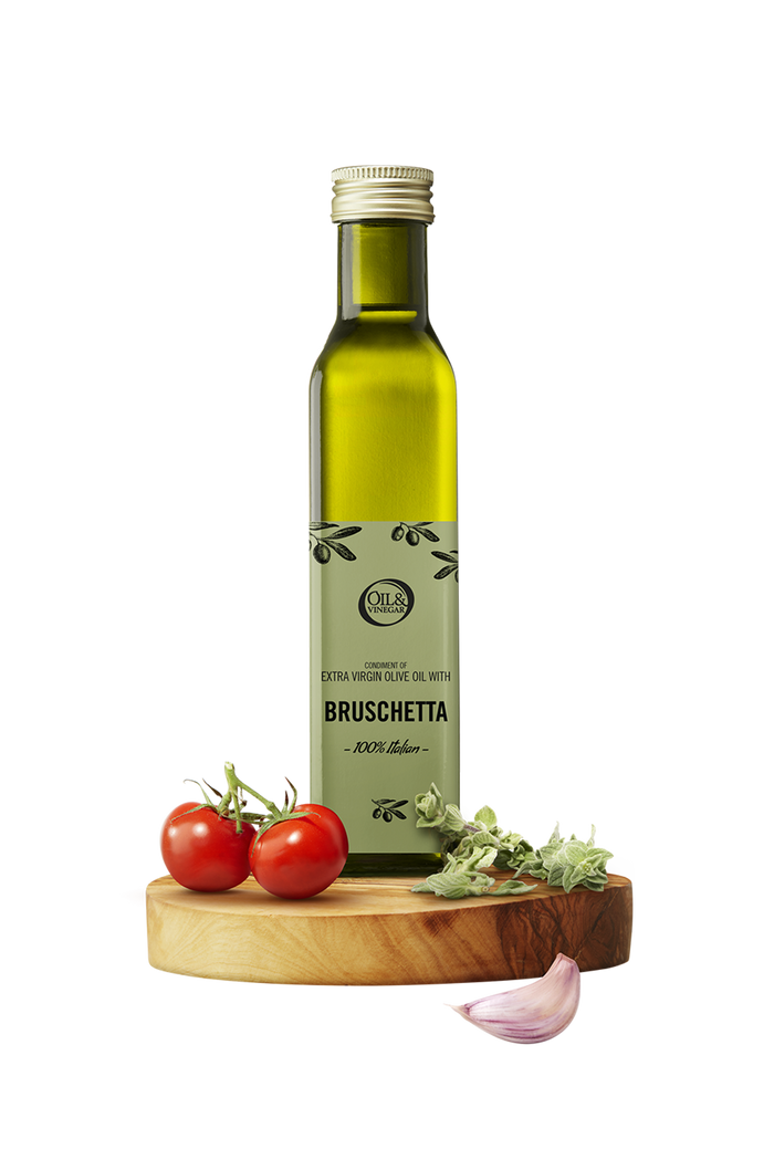Green bottle of olive oil with a label stating the flavor as bruschetta on a wooden stand with tomatoes and herbs