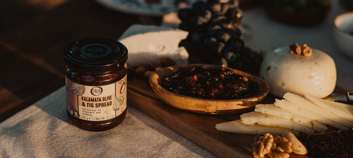 Jar of kalamata olive and fig spread with a black lid next to a charcuterie board with cheese and the jam in a small dish