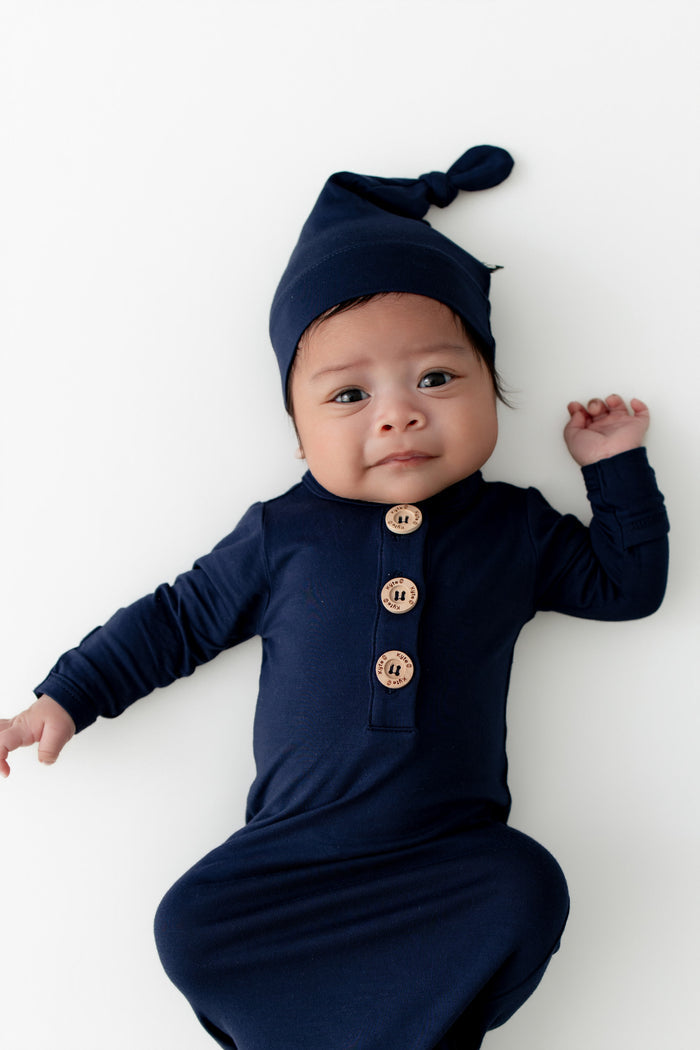Baby wearing a navy blue outfit with buttons and matching hat on a white background