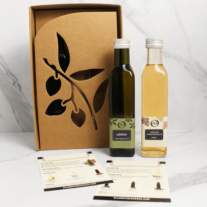 Two bottles of one olive oil and one vinegar a box with an olive branch design on a white background