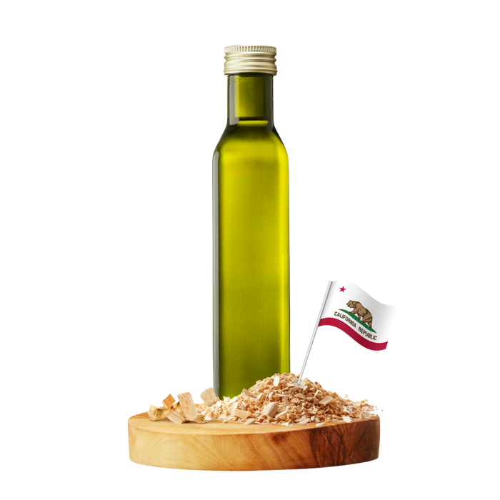 A tall olive-green glass bottle with a silver cap stands on a round wooden board with several wood chips and a small California flag.