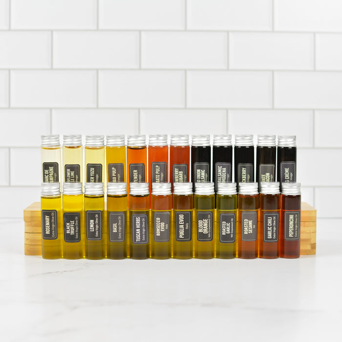 two Rows of small bottles of oils and vinegars with labels on a white tiled wall background