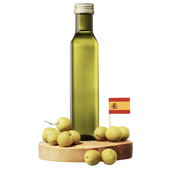 A clear bottle of Arbequina Extra Virgin Olive Oil with a wooden base, surrounded by small green olives and a small Spanish flag.