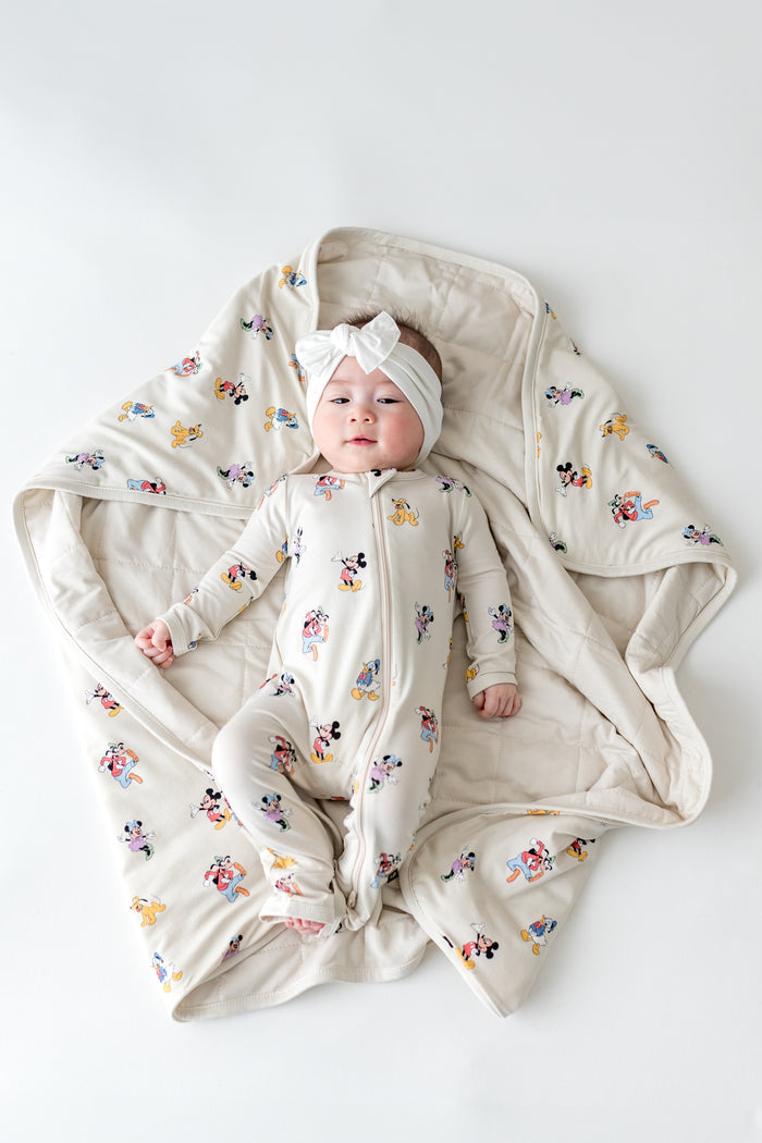 Baby wearing a Mickey Mouse footie laying on a matching baby blanket