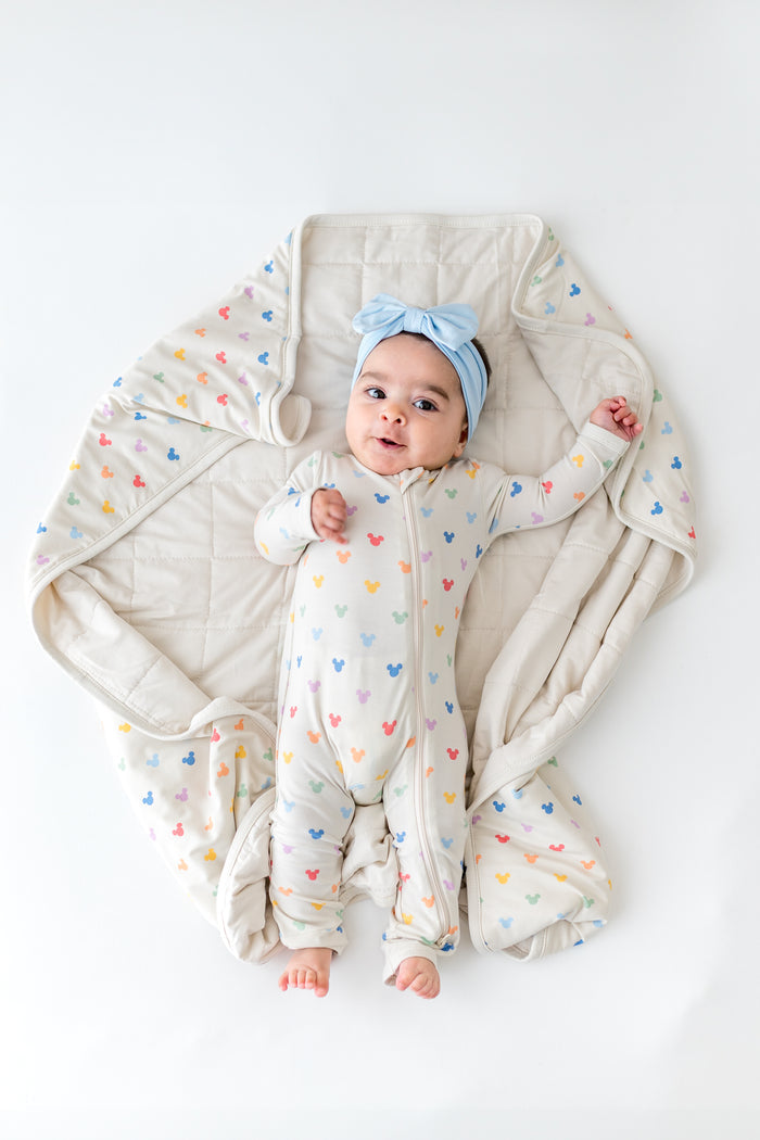 Baby in a pastel Mickey Mouse head romper laying on a matching print blanket