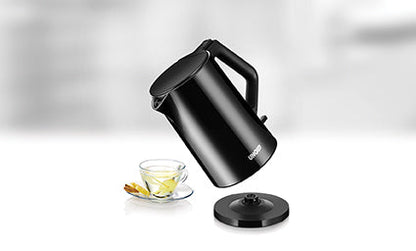 Der Unold Blitzkocher Design 1,4 L in schlichtem Schwarz steht schräg über einer Teetasse aus Glas mit Zitronenscheibe, neben seinem runden Sockel auf einer weißen Fläche mit unscharfem Hintergrund.