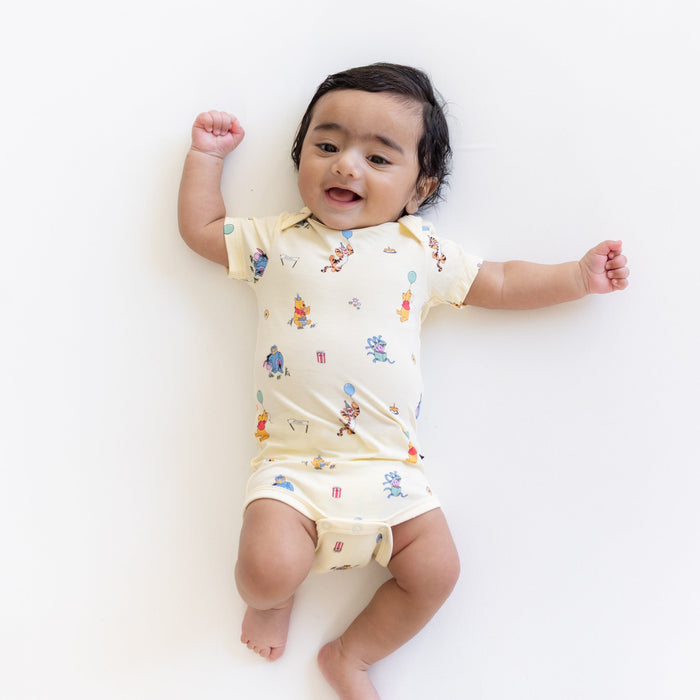 Infant laying on a light neutral surface wearing the Bodysuit in Winnie the Pooh Celebration