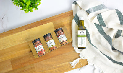 Bottle of olive oil and three spice containers on a wooden board with a white and green striped towel.