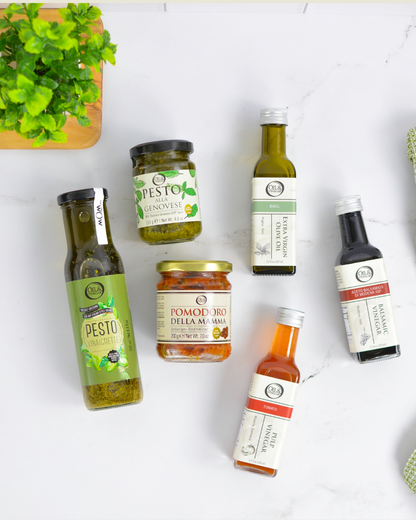 Collection of pesto and tomato products on a white surface with a plant in the corner.