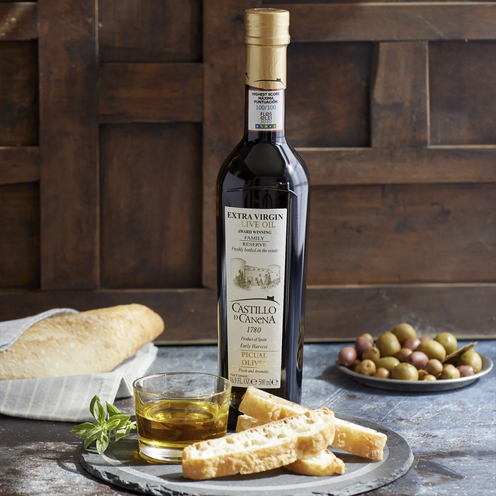 Bottle of castillo de canena olive oil on a tablescape with bread and olives