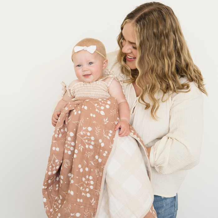 Mom holding baby girl snuggled with Simple Buds Cotton Muslin 4-Layer quilt.