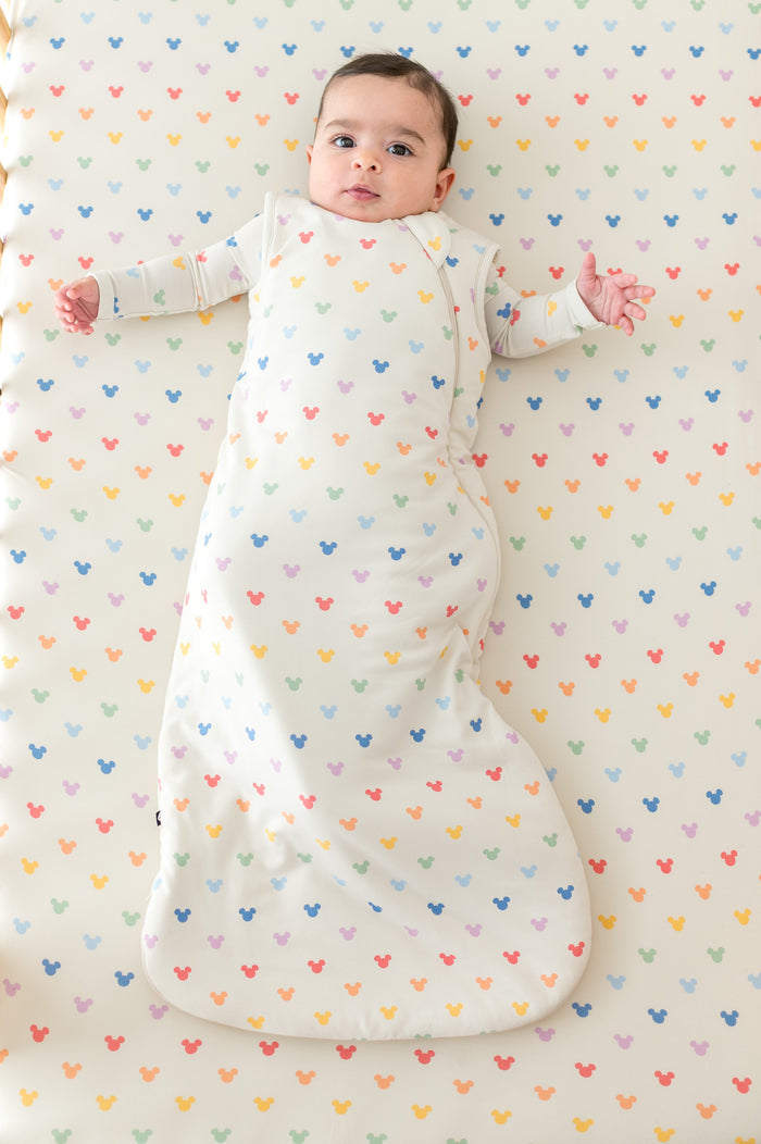Baby in a crib with pastel mickey mouse head pattern and wearing a matching sleep sack