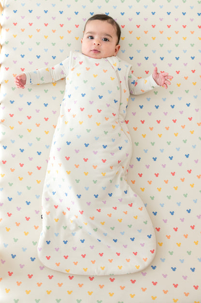Baby in a crib with pastel mickey mouse head pattern and wearing a matching sleep sack