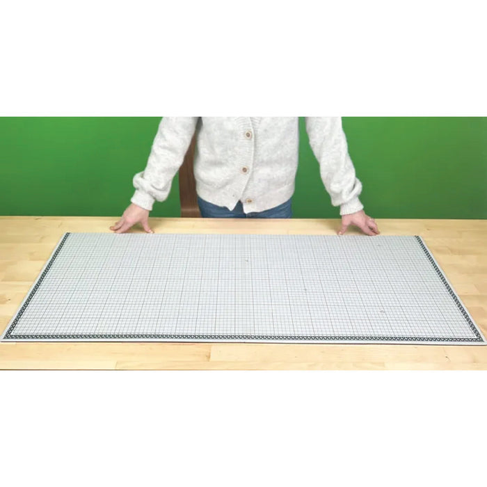 Person standing behind a large grid mat on a wooden surface with a green background