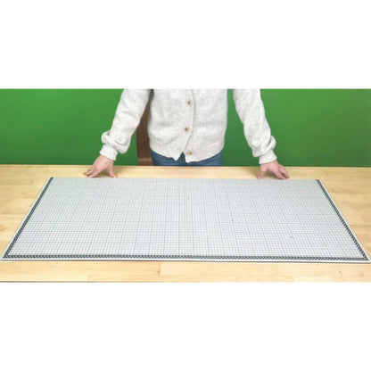 Person standing behind a large grid mat on a wooden surface with a green background
