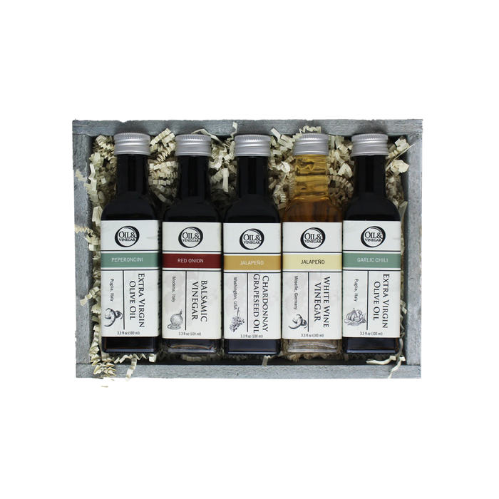 Set of five olive oil and vinegar bottles in a wooden box with decorative elements.