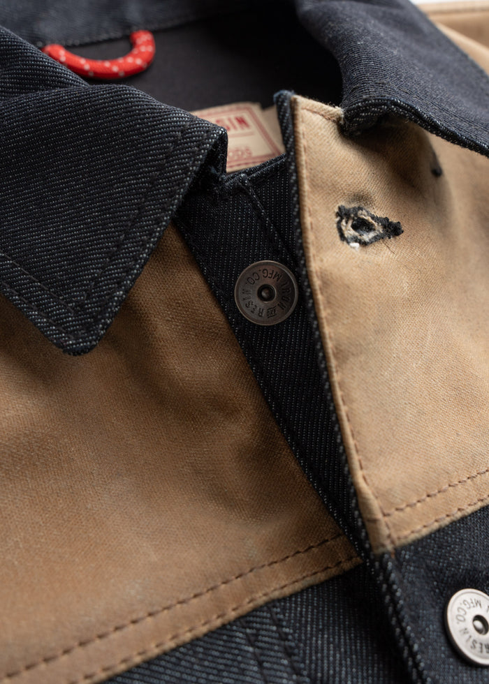 Close-up of a denim and canvas jacket with a visible button and red hanger. The fabric shows a small tear near the collar.