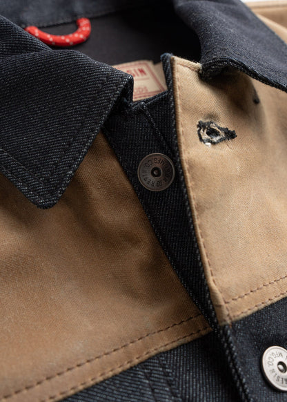 Close-up of a denim and canvas jacket with a visible button and red hanger. The fabric shows a small tear near the collar.
