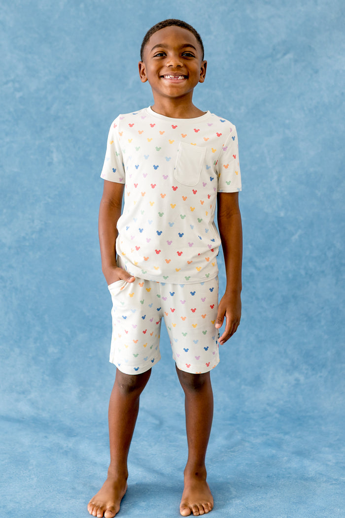 Child wearing a cream outfit with colorful mickey head patterns against a blue background
