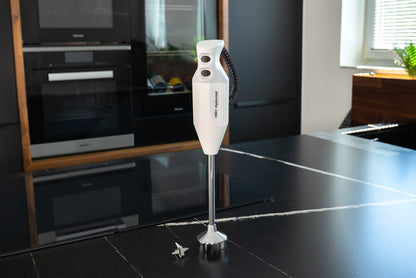 Der Unold ESGE-Zauberstab® P 350 Profi, ein weißer Stabmixer, steht aufrecht auf einer schwarzen Arbeitsplatte in einer modernen Küche, der kleine Metallklingenaufsatz liegt daneben.