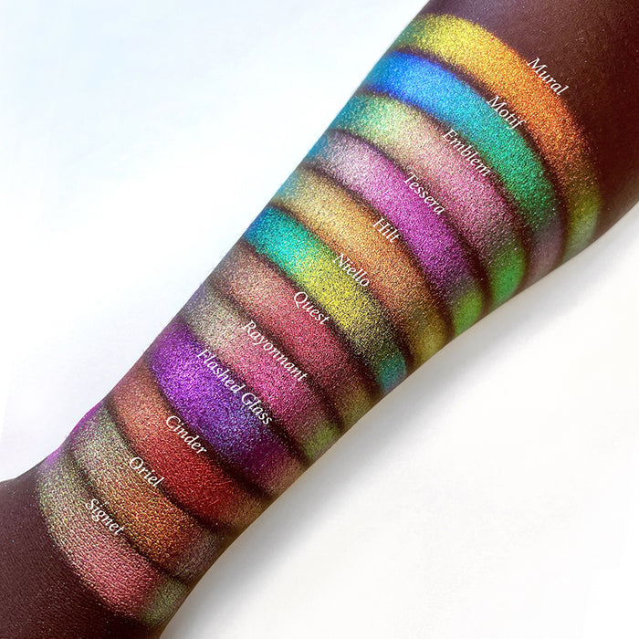 Top angled arm swatches on deep skin tone of Flashed Glass Electric Multichrome Pigment shifts compared to Mural, Motif, Emblem, Tessera, Hilt, Niello, Quest, Rayonnant, Cinder, Oriel and Signet
