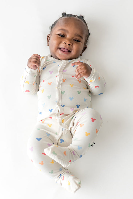 Baby wearing a cream-colored footie with colorful mickey patterns on a white background