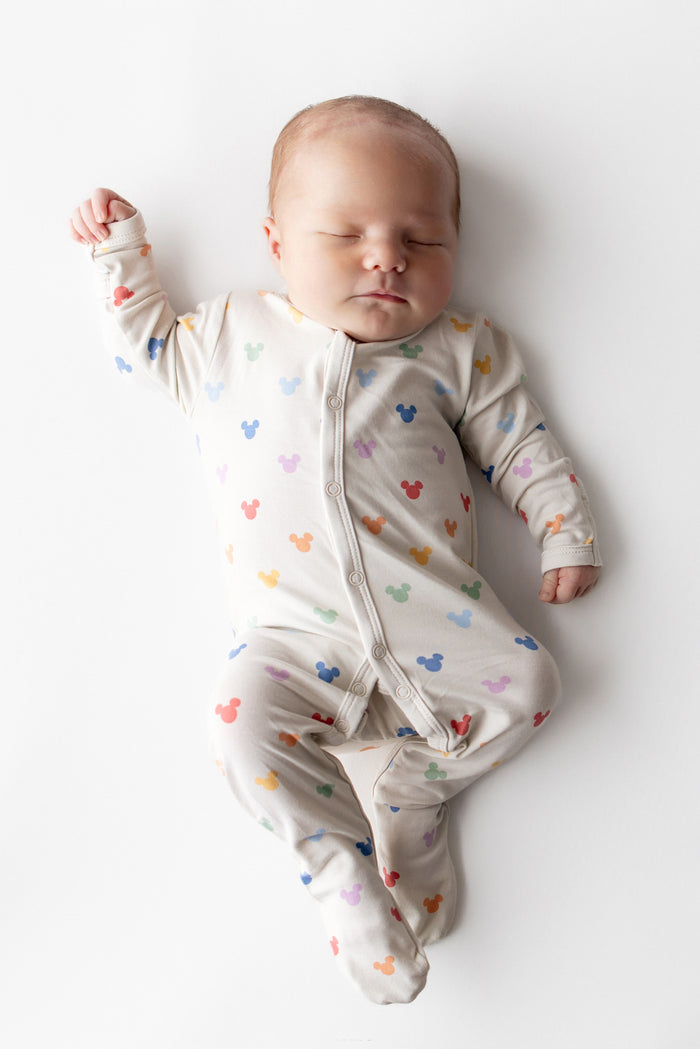Baby wearing a colorful onesie with mickey head patterns on a white background