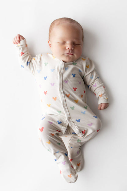 Baby wearing a colorful onesie with mickey head patterns on a white background