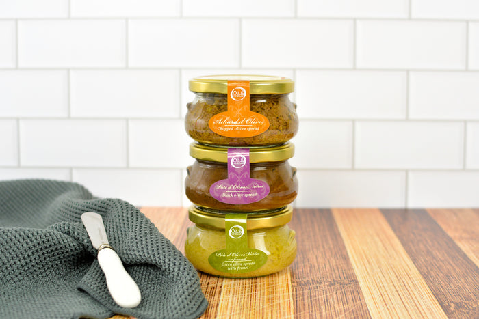 three flat jars of olive spreads with different flavors with gold lids stacked on each other
