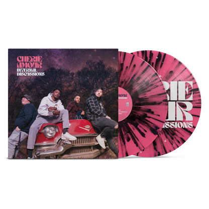 We see a vinyl cover with a picture of the band members sitting on an old 50s Cadillac. It is nighttime in the middle of winter and the stars are visible behind the band. In the top left corner there is text that reads Cherie Amour Internal Discussions. Sticking out of the vinyl cover is two vinyl's both colored pink and black.
