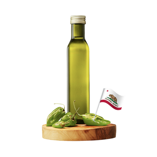 A tall olive-green glass bottle with a silver cap stands on a round wooden board with several green chili peppers and a small California flag.