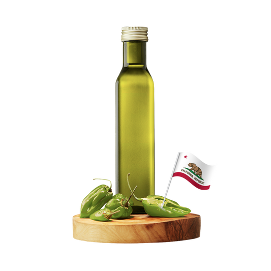 A tall olive-green glass bottle with a silver cap stands on a round wooden board with several green chili peppers and a small California flag.