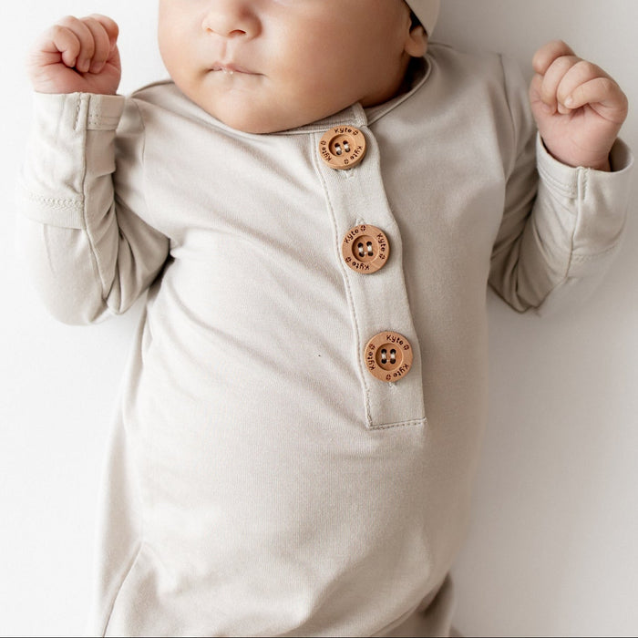 Close up of Baby in oat colored knotted gown outfit that has wooden buttons and a matching hat