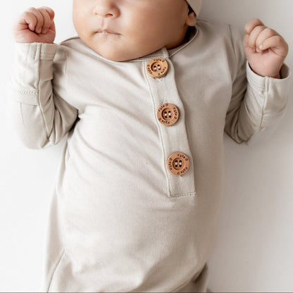 Close up of Baby in oat colored knotted gown outfit that has wooden buttons and a matching hat