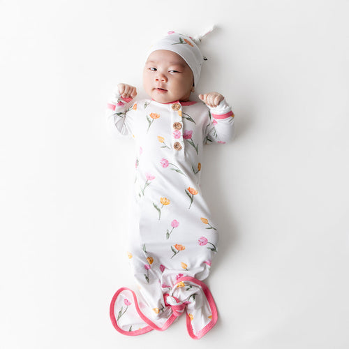 Newborn laying on a white surface wearing the Knotted Gown with Hat Set in Tulip