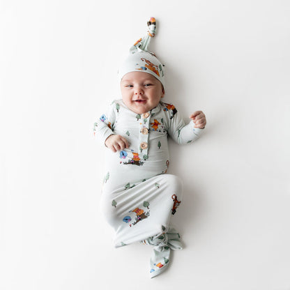 Young infant wearing the Knotted Gown with Hat Set in Winnie the Pooh Hundred Acre Wood laying on a light surface