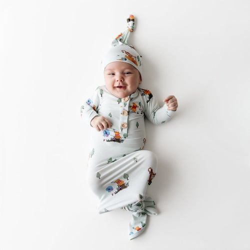 Young infant wearing the Knotted Gown with Hat Set in Winnie the Pooh Hundred Acre Wood laying on a light surface