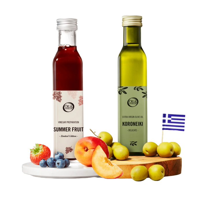 Two bottles of 'Summer Fruit' vinegar and 'Koroneiki' olive oil on a wooden board with fruits, and a Greek flag in the corner.