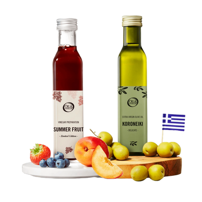 Two bottles of 'Summer Fruit' vinegar and 'Koroneiki' olive oil on a wooden board with fruits, and a Greek flag in the corner.