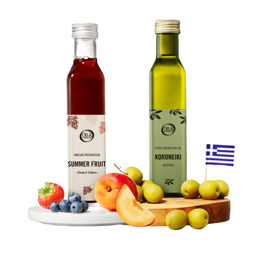 Two bottles of 'Summer Fruit' vinegar and 'Koroneiki' olive oil on a wooden board with fruits, and a Greek flag in the corner.