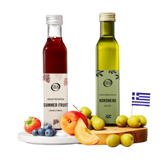 Two bottles of 'Summer Fruit' vinegar and 'Koroneiki' olive oil on a wooden board with fruits, and a Greek flag in the corner.