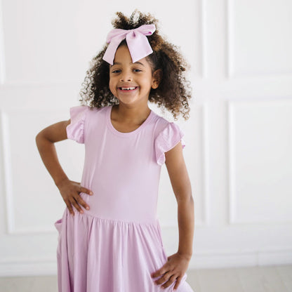 Young girl posing wearing the Large Alligator Clip Bow in Thistle with matching pocket dress