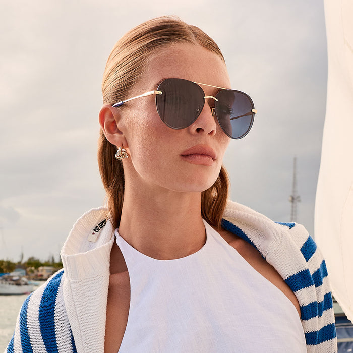 lifestyle - blonde female on a boat wearing diff eyewear lenox aviator sunglasses with a gold metal frame and blue gradient polarized lenses angled view
