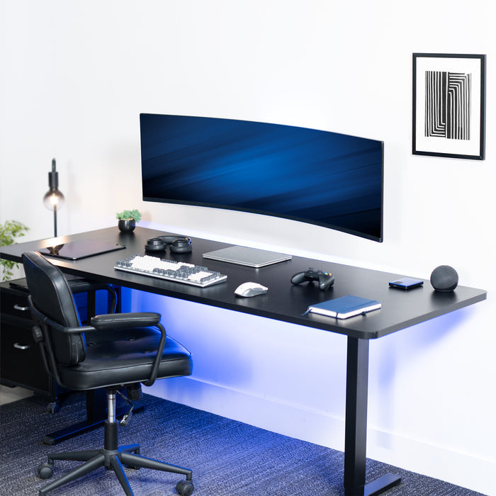 Modern office desk setup with a large monitor, chair, and various items on a white wall background.