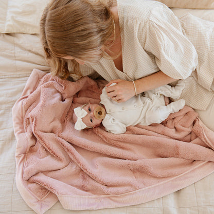 A mother holds her baby girl in a Luxury Receiving Ballet Slipper (light pink) Colored Lush Saranoni Blanket. The soft blanket is a small blanket and a baby blanket or toddler blanket.