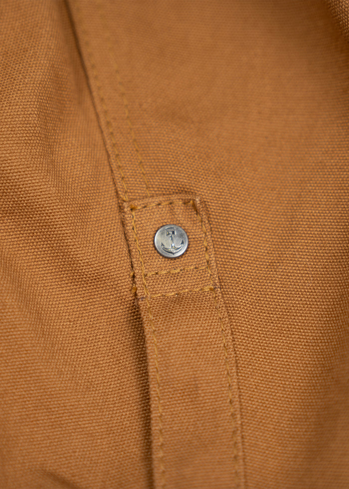Close-up of a brown fabric with a metal button, showcasing detailed stitching and texture, highlighting craftsmanship.