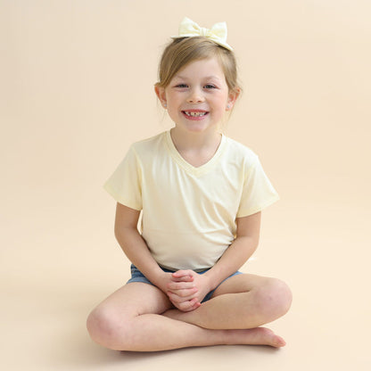 Young smiling girl sitting cross legged on the floor wearing the Medium Alligator Clip Bow in Chamomile with a matching shirt