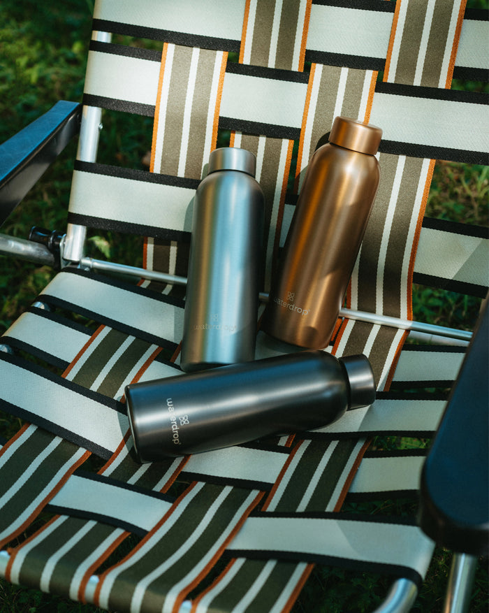 Metal Thermo Steel drinking bottles on a striped outdoor chair. The bottles feature a brushed metal look, designed to keep drinks cold for 24 hours or hot for 12 hours.