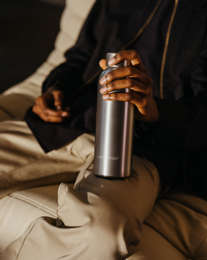 Person holding Metal Thermo Steel bottle with a brushed metal finish, designed to keep drinks cold for 24 hours or hot for 12 hours.